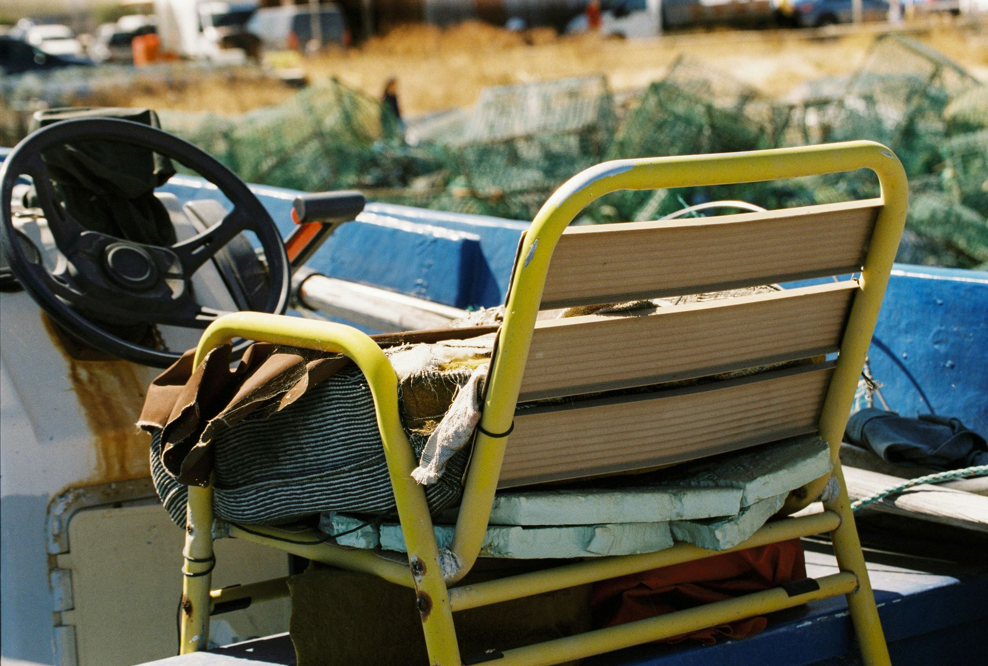 A worn yellow deck chair on a blue fishing boat beside a steering wheel